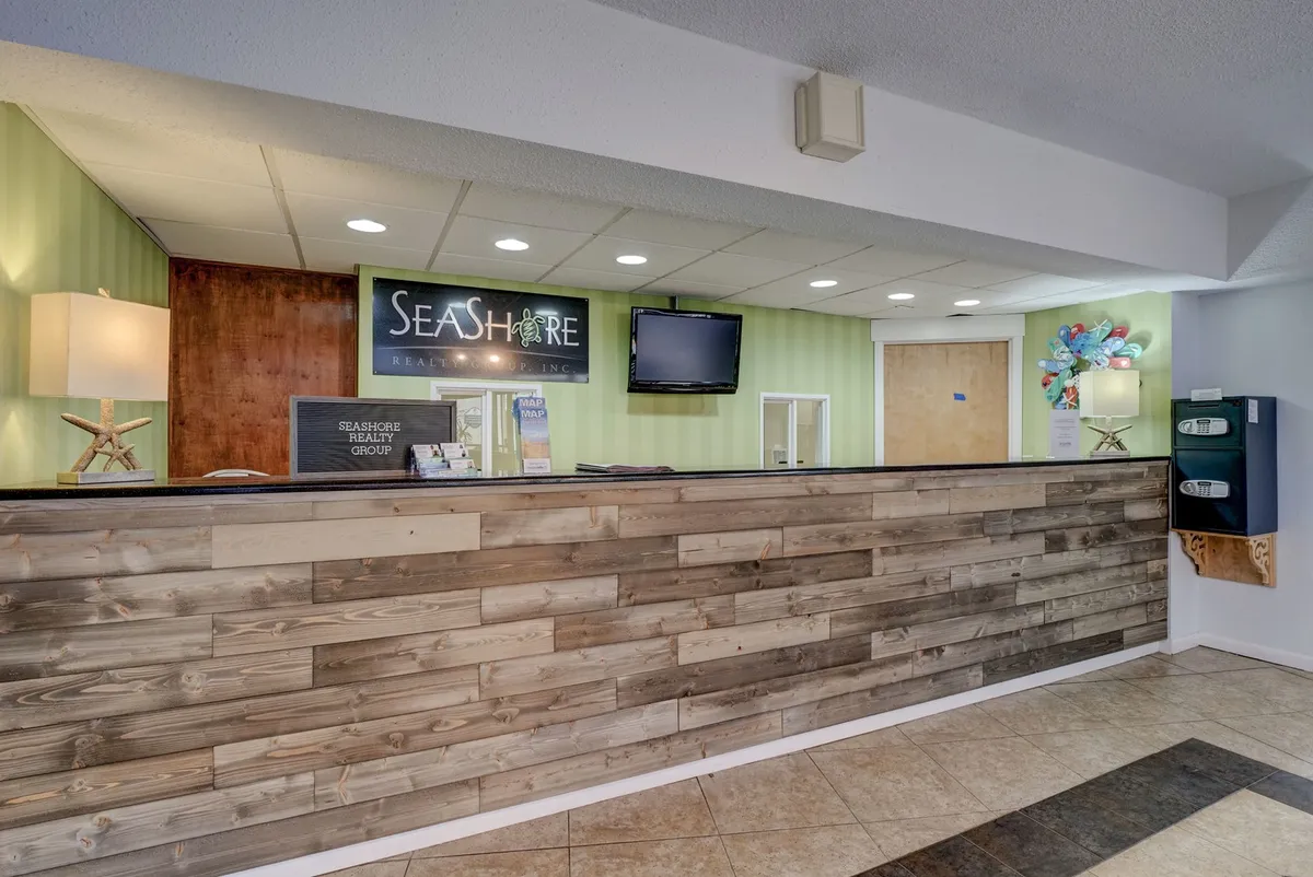 A welcoming reception area featuring a reception desk, a 'SEASHORE' sign, and a starfish-base lamp, creating a friendly and approachable environment for onsite check-in and guest support.