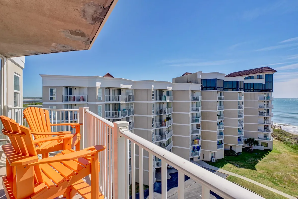 A private balcony with striking ocean views, two orange chairs arranged for relaxation, and a sturdy railing. The space is bathed in natural light, inviting guests to sit and savor the coastal atmosphere morning or night.