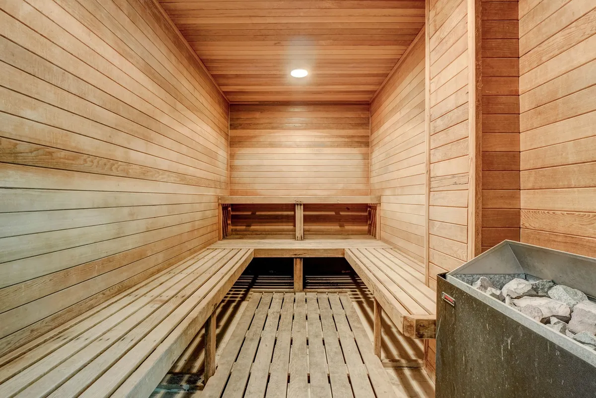 A serene sauna with wooden benches and walls, accompanied by a stone heater, inviting relaxation and post-workout rejuvenation.