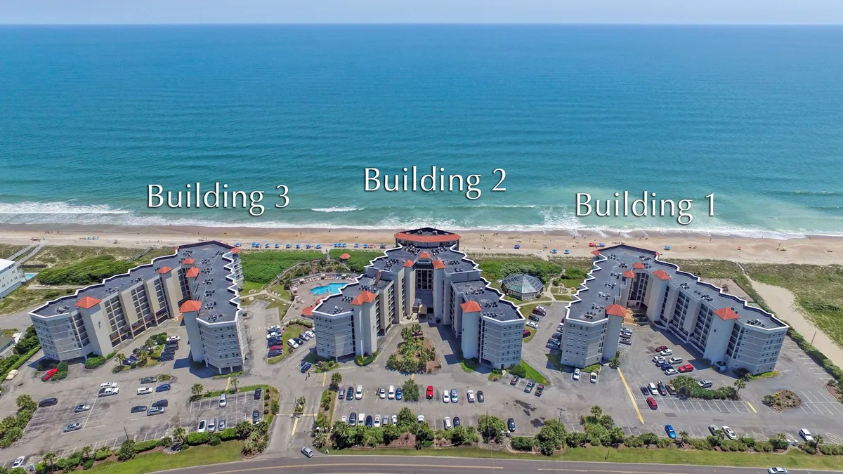 This exterior shot captures three resort buildings with a sparkling swimming pool in the foreground and the ocean just beyond. The composition highlights the proximity of both the pool and beach, inviting guests to unwind and take in the coastal surroundings.