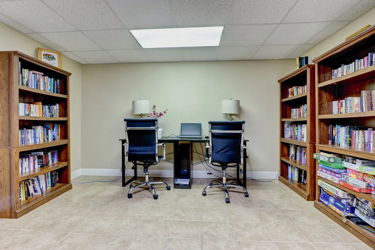 A serene community business center lined with bookshelves packed with books, individual desks with comfortable chairs, and desk lamps providing warm lighting. The overall feel is quiet, organized, and conducive to productivity and correspondence.