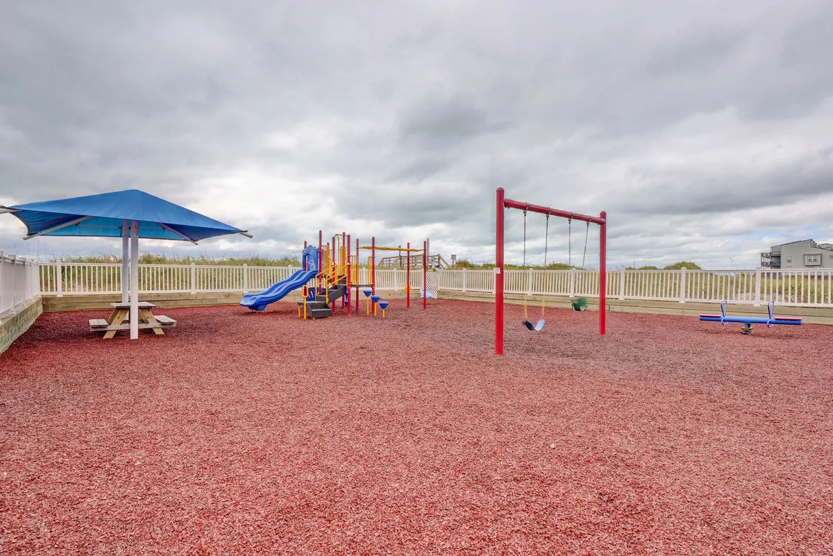 A vibrant playground equipped with swings and climbing structures, adjacent to a picnic area, where children can play and families can gather outdoors.